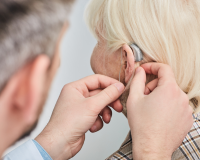 Audiologist fits hearing aid into senior woman's ear