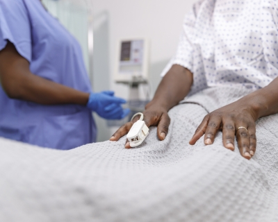 A nurse assists a patient on a hospital bed with a pulse oximeter