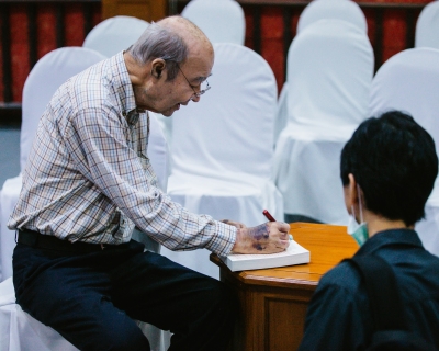 Mechai Viravaidya, aka &quot;Mr. Condom,&quot; signs a copy of his biography, From Condoms to Cabbages, for a visitor from the International Conference on Family Planning at the Cabbages and Condoms restaurant in Pattaya, Thailand. 